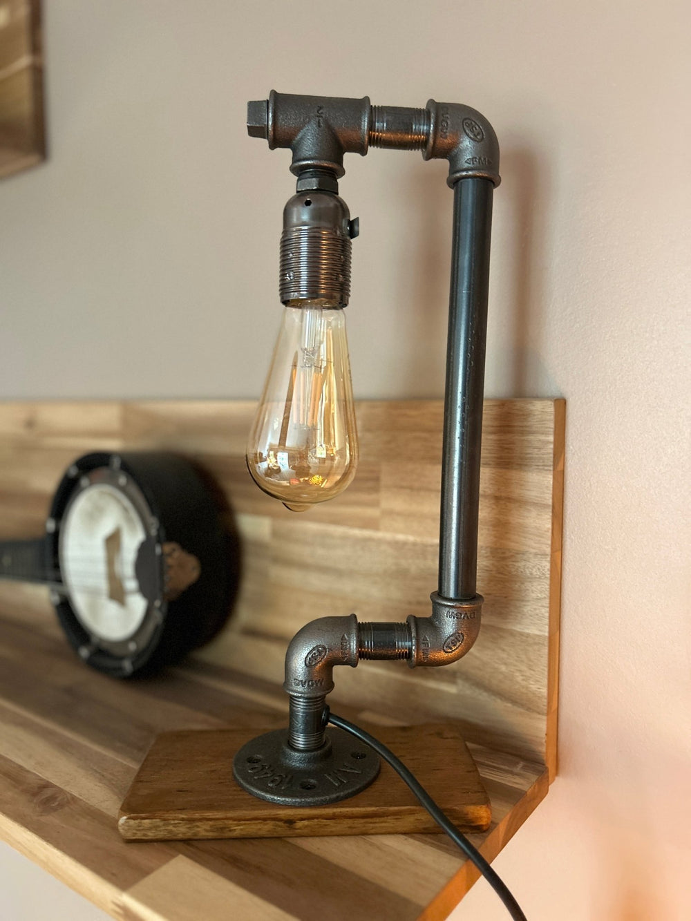 An industrial style pipework table lamp featuring a bulb resembling a drop of water, placed in a home environment.