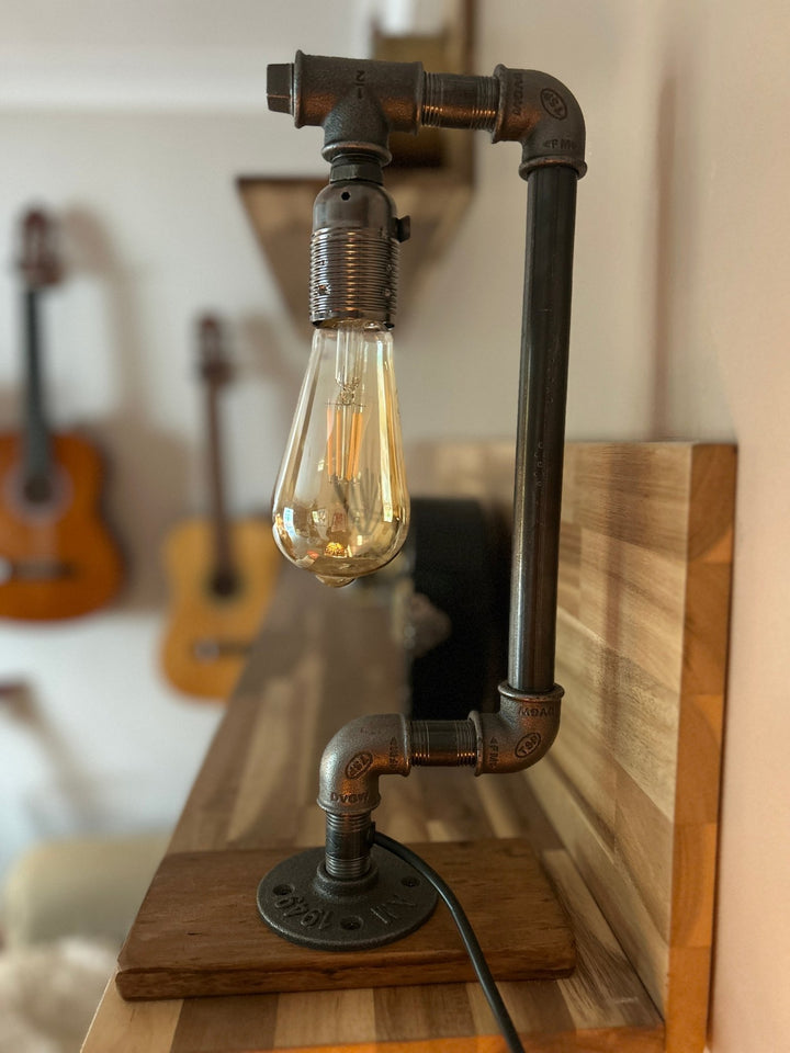 industrial style table lamp with pipe structure and wooden base, a bulb resembling a drop of water, shown in a home