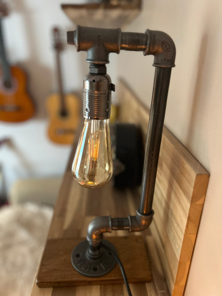 industrial style table lamp with pipe structure and wooden base, a bulb resembling a drop of water, shown in a home