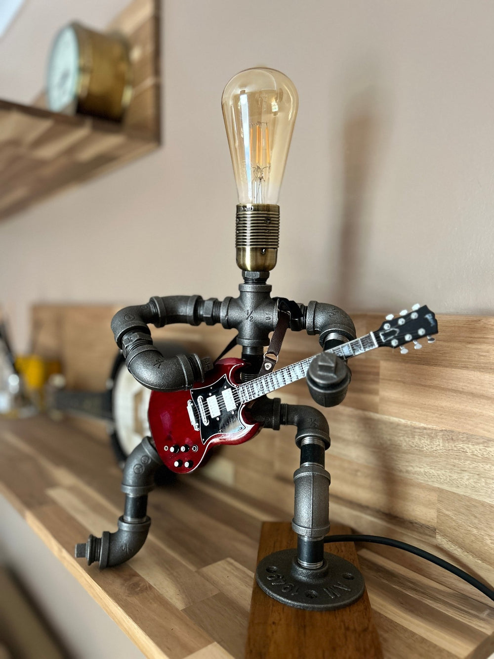 Pipework Guitar lamp holding a replica AC/DC miniature guitar on a wooden shelf