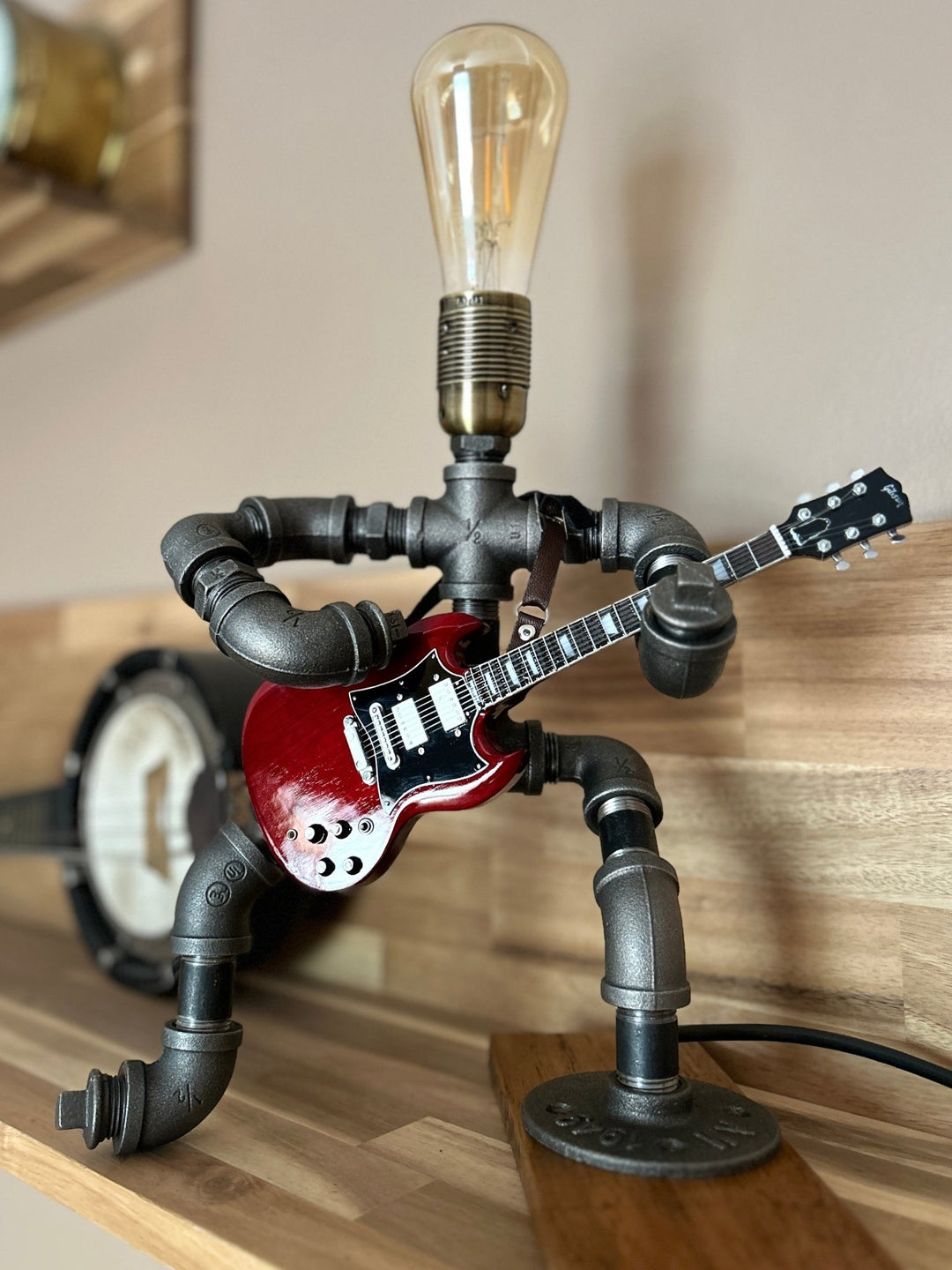 Pipework Guitar lamp holding a replica AC/DC miniature guitar on a wooden surface