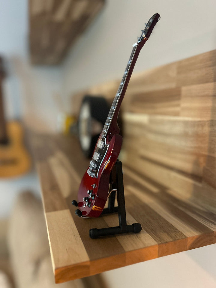 Red electric miniature ACDC guitar on a wooden surface shown side on