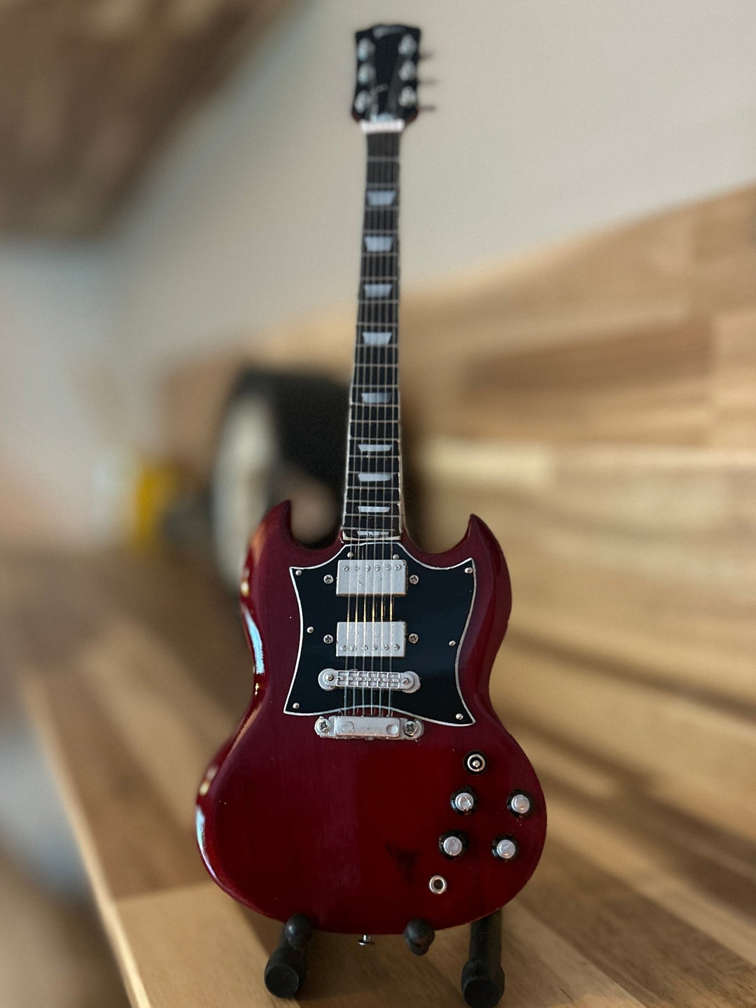 Red electric miniature ACDC guitar on a wooden surface with a blurred background