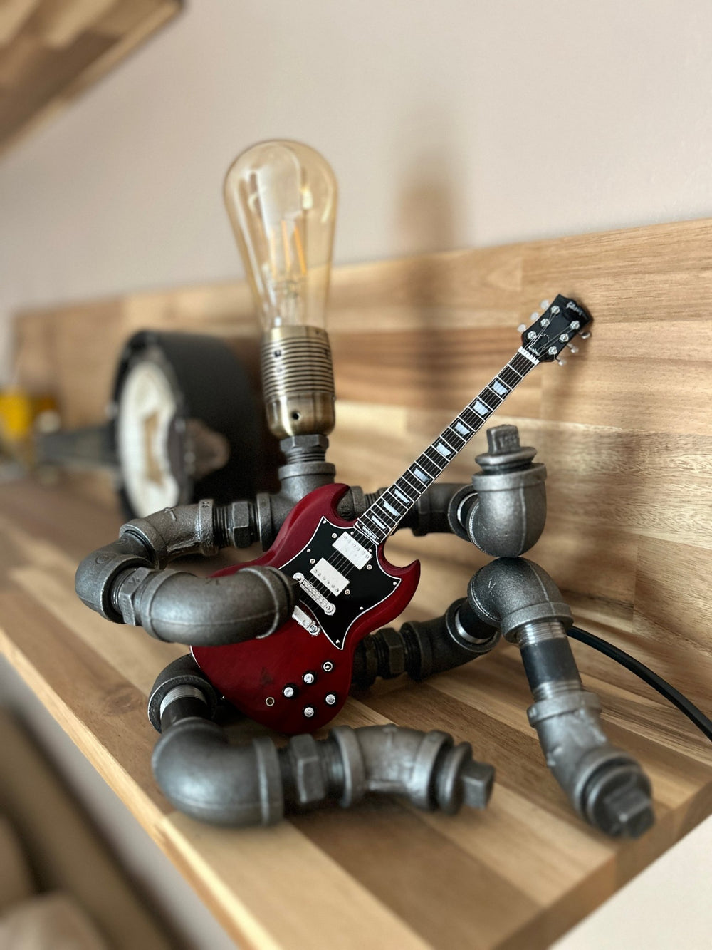 Pipework seated Guitar lamp holding a replica AC/DC miniature guitar on a wooden surface