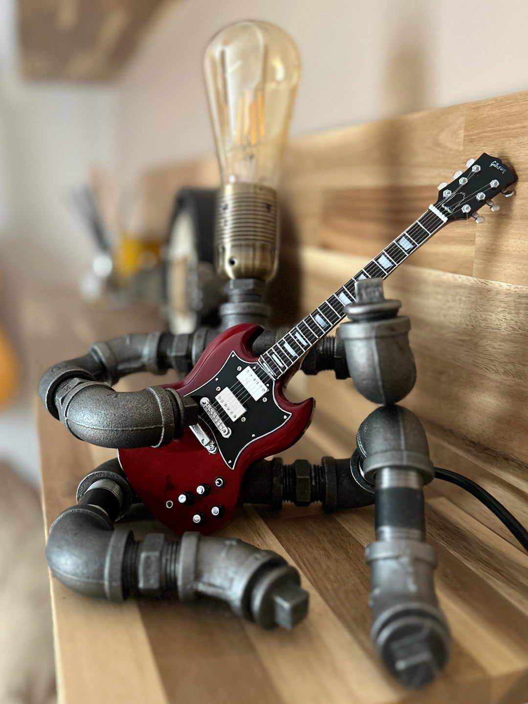 Pipework seated Guitar lamp holding a replica AC/DC miniature guitar on a wooden surface