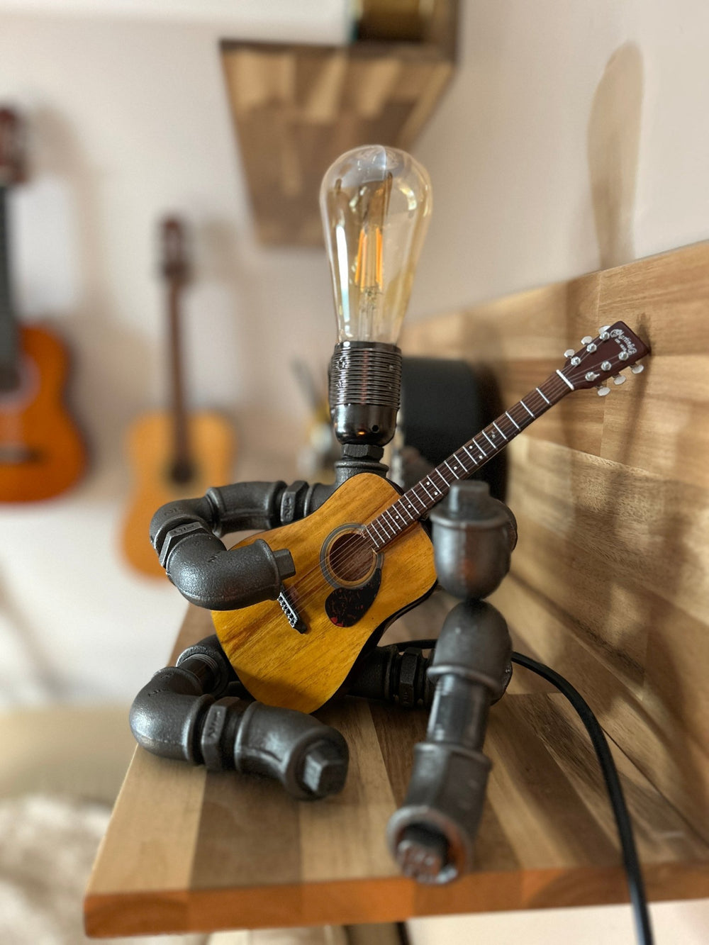 Industrial style pipework guitar lamp holding a miniature acoustic guitar with a light bulb