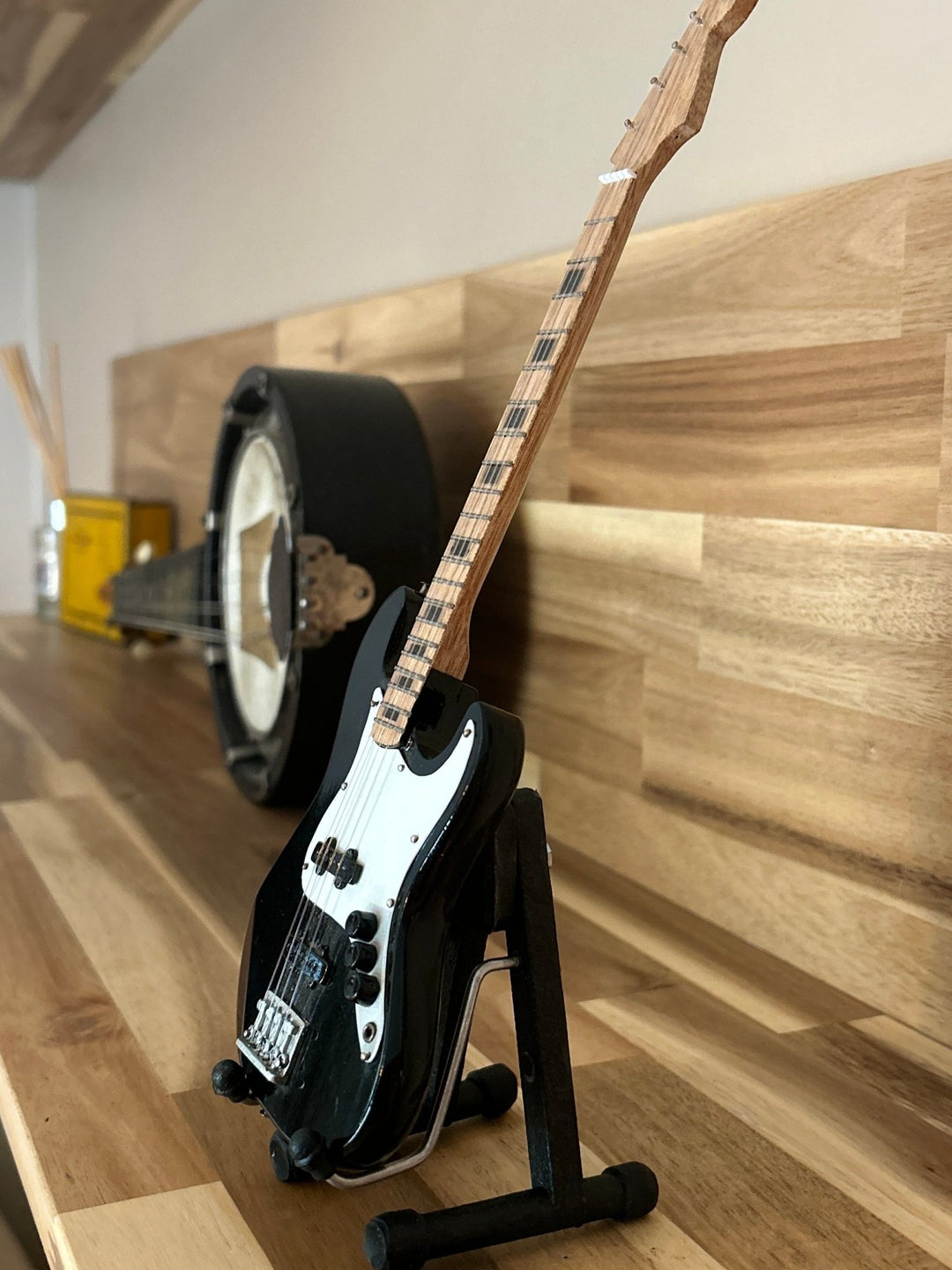 Black Electric miniature guitar on a stand against a wooden wall
