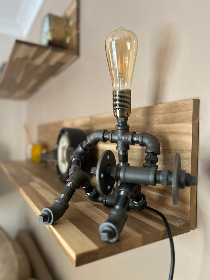 Industrial-style pipework table lamp in stance of a weightlifter with dumbbell on shelf
