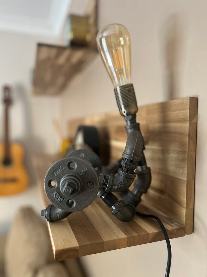 Industrial-style pipework table lamp in stance of a weightlifter with dumbbell shown from side