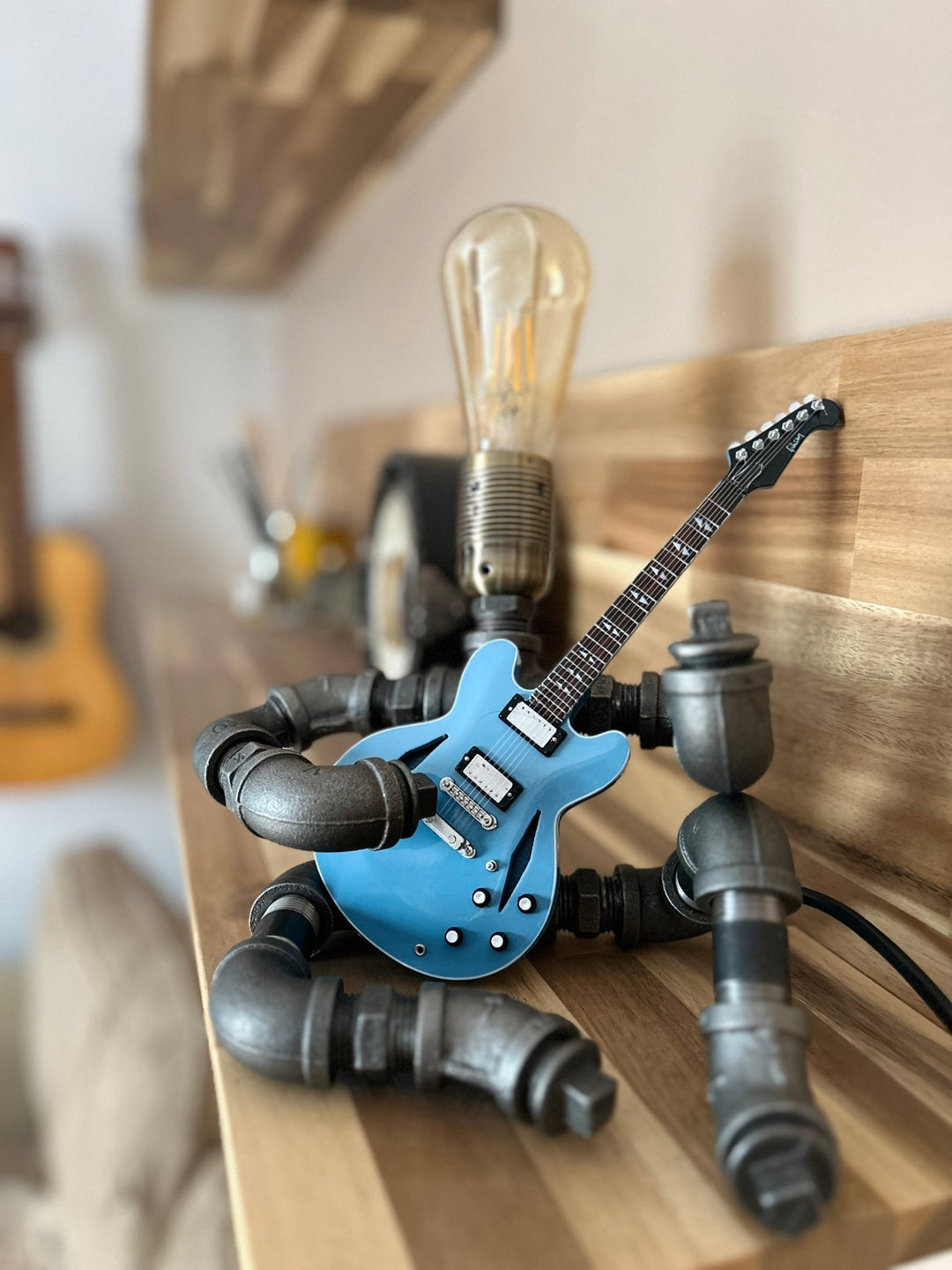 Pipework Guitar lamp holding a Foo Fighters inspired miniature guitar on a wooden shelf