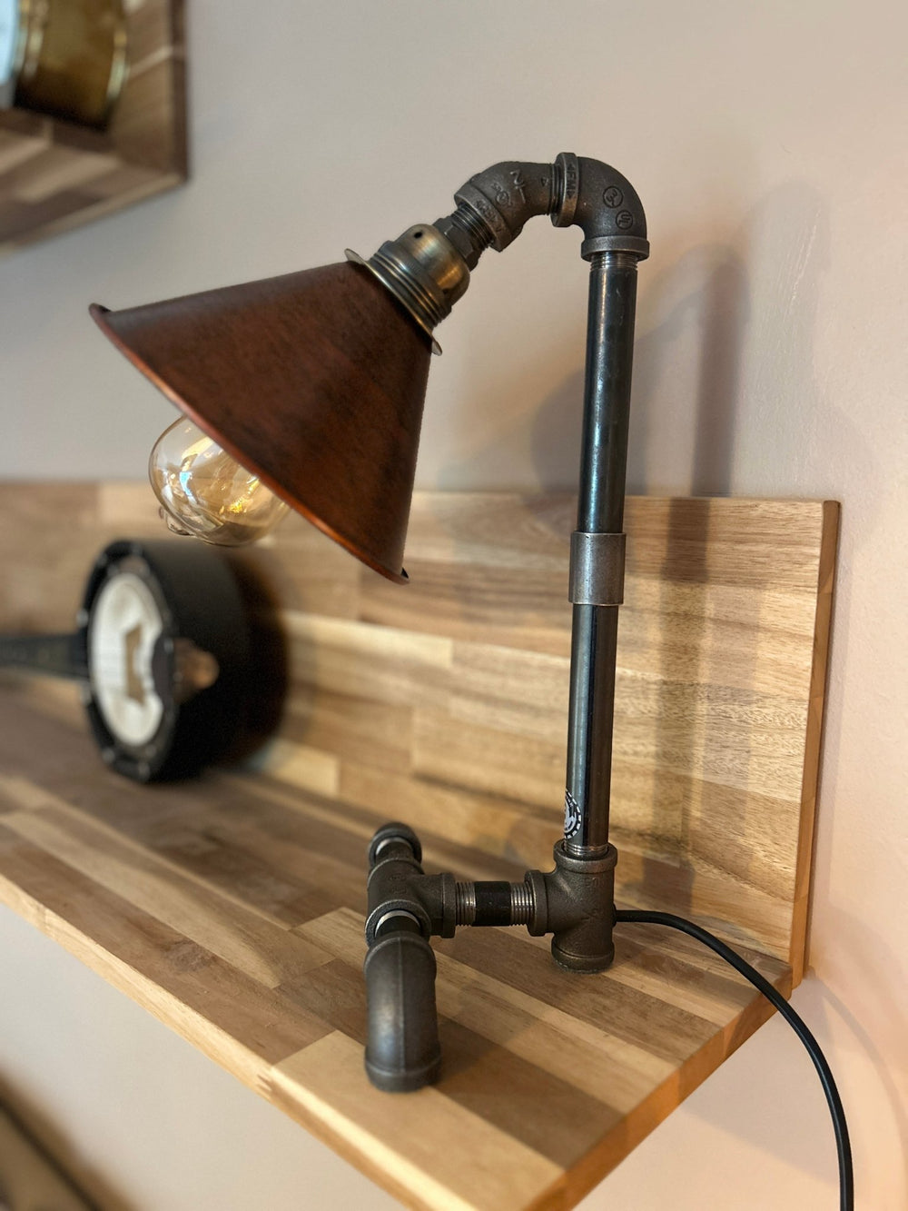 Industrial-style pipework bedside table lamp with a copper coloured shade on a wooden shelf