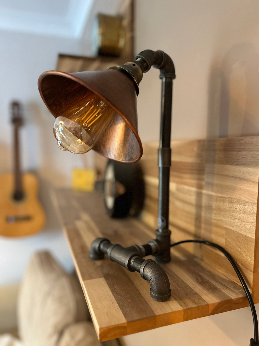  industrial style bedside lamp from pipework with copper coloured shade on a wooden shelf