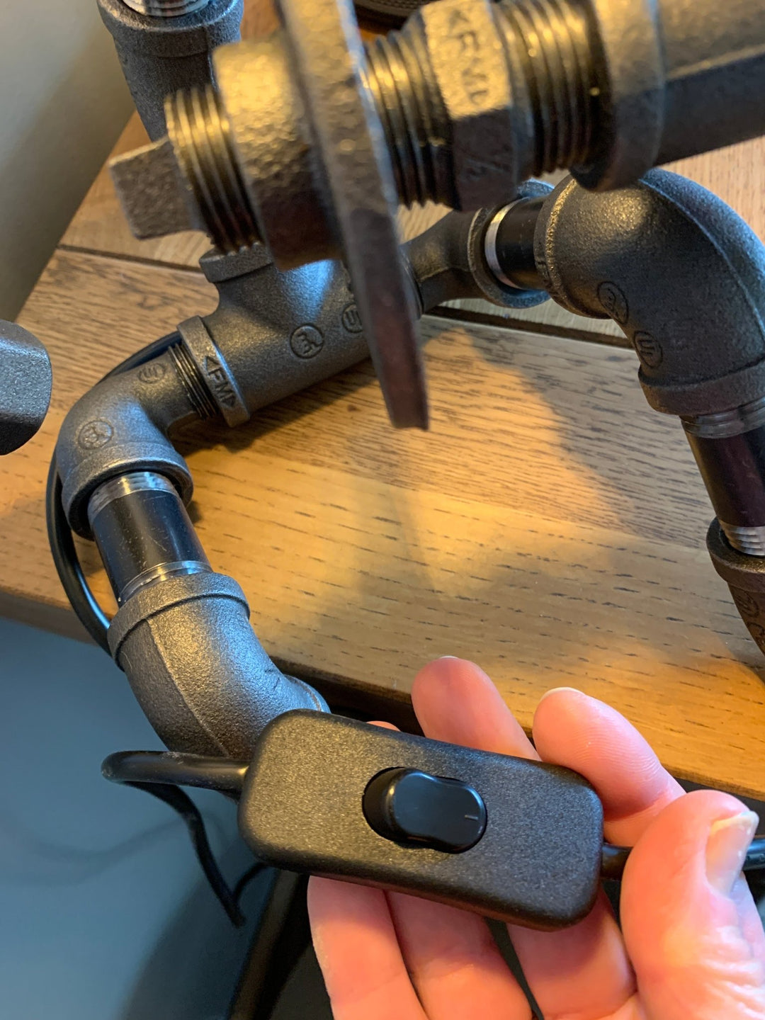 Hand holding a black inline switch next to pipework lamps on a wooden surface