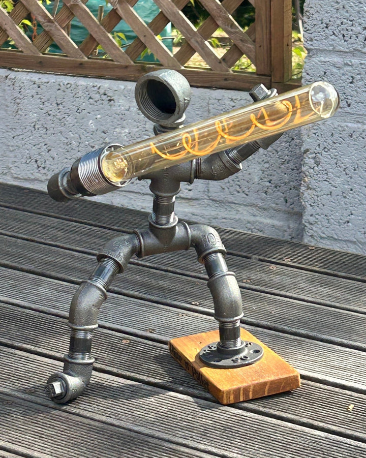 Decorative pipework lamp in the stance of a Jedi Knight holding a long bulb to imitate a lightsaber shown outside