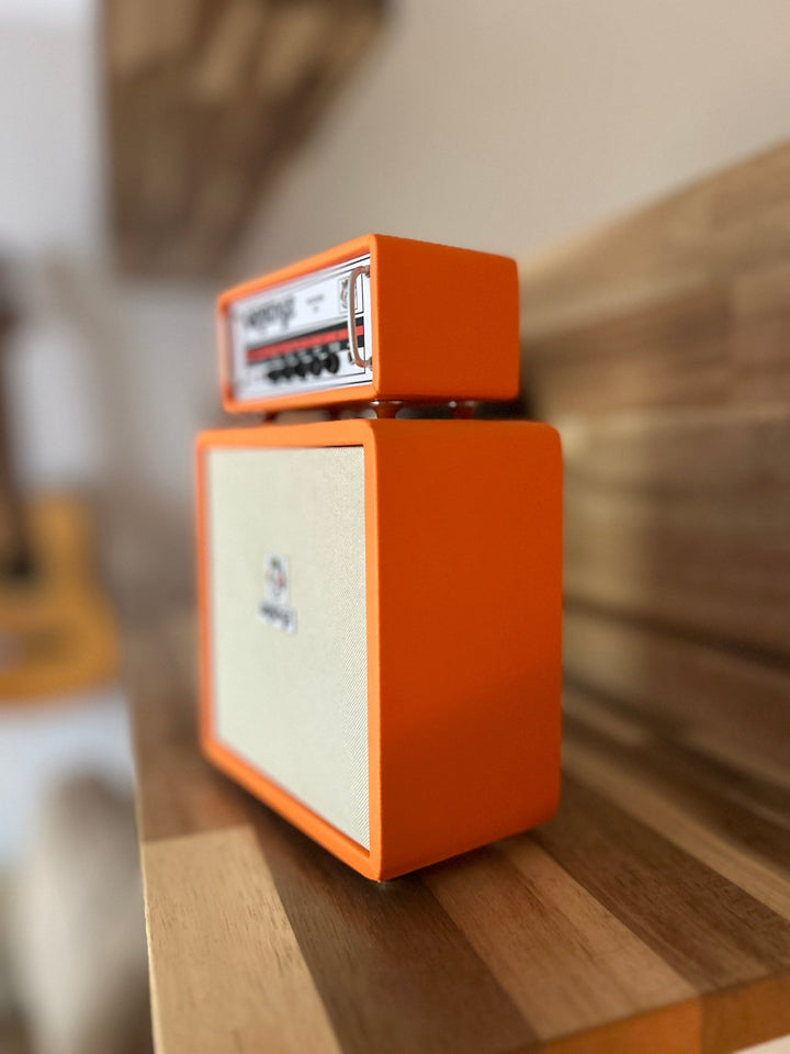 A handcrafted miniature orange-colored Orange brand amplifier, featuring a speaker cabinet and a control panel with knobs and branding, shown as a side angle
