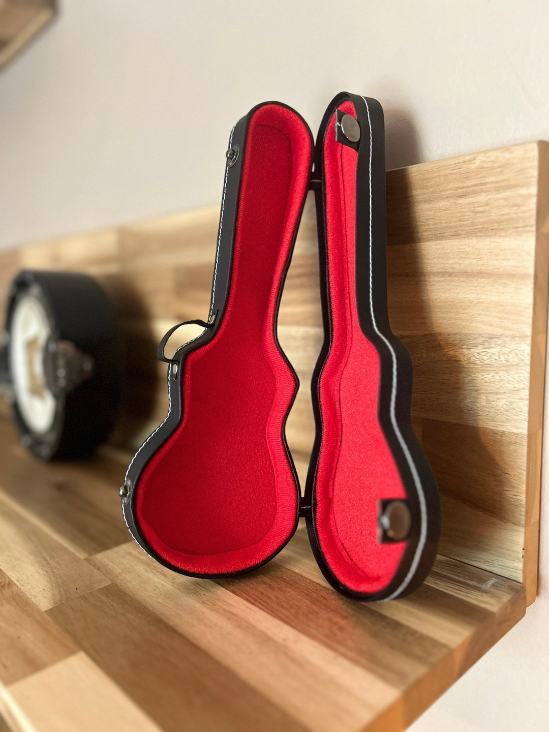 Red miniature guitar case with black trim open on a wooden shelf