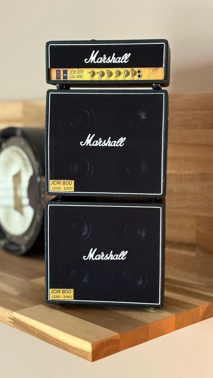 Miniature Marshall amplifier stack on a wooden surface with a blurred ukelele in the background