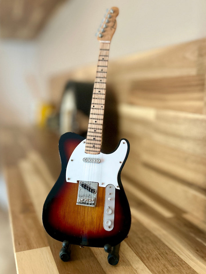 miniature Radiohead replica guitar on a wooden surface with a blurred background
