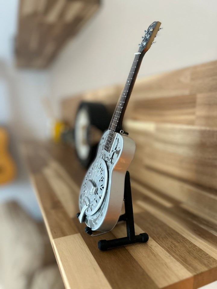 miniature resonator guitar model on a stand against a wooden background