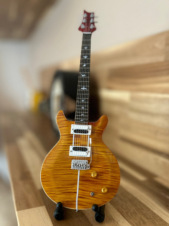 miniature Santana replica guitar on a wooden surface with a blurred background