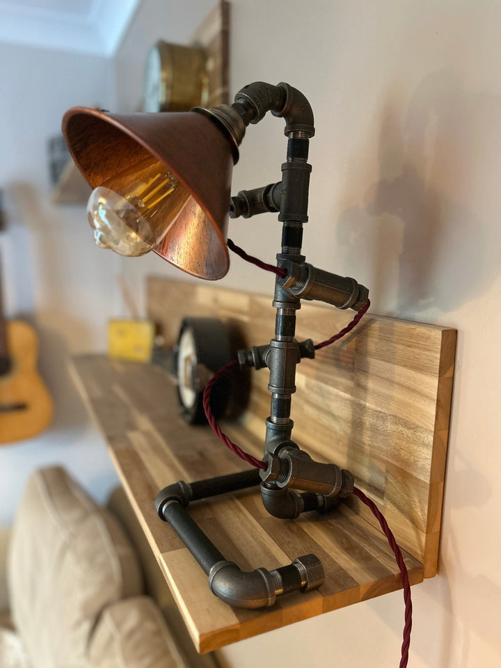 Pipework Lamp with braided burgundy cord spiralling around the lamp with copper coloured shade on a wooden shelf