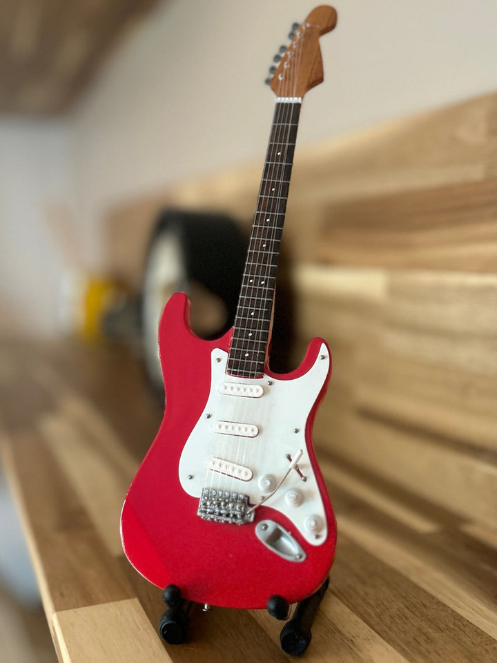 Red electric miniature Stratocaster guitar on a wooden surface with a blurred background