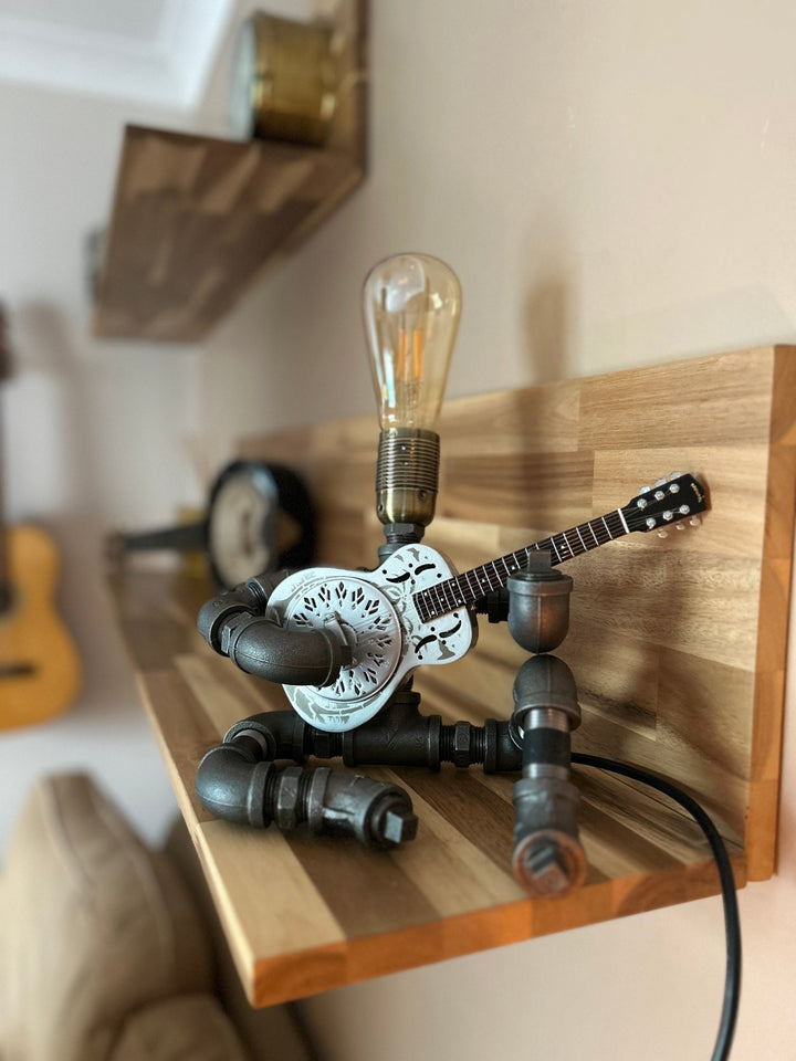 Pipework Guitar lamp holding a resonator inspired miniature guitar on a wooden shelf