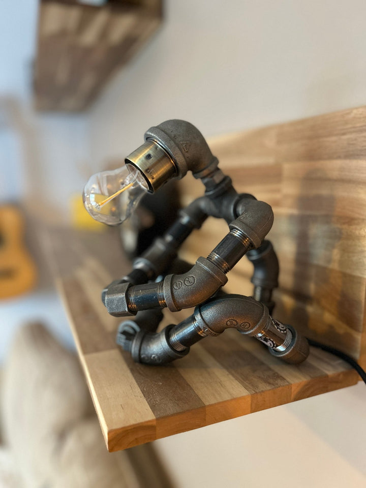 Industrial-style pipework robot lamp on a wooden shelf side view