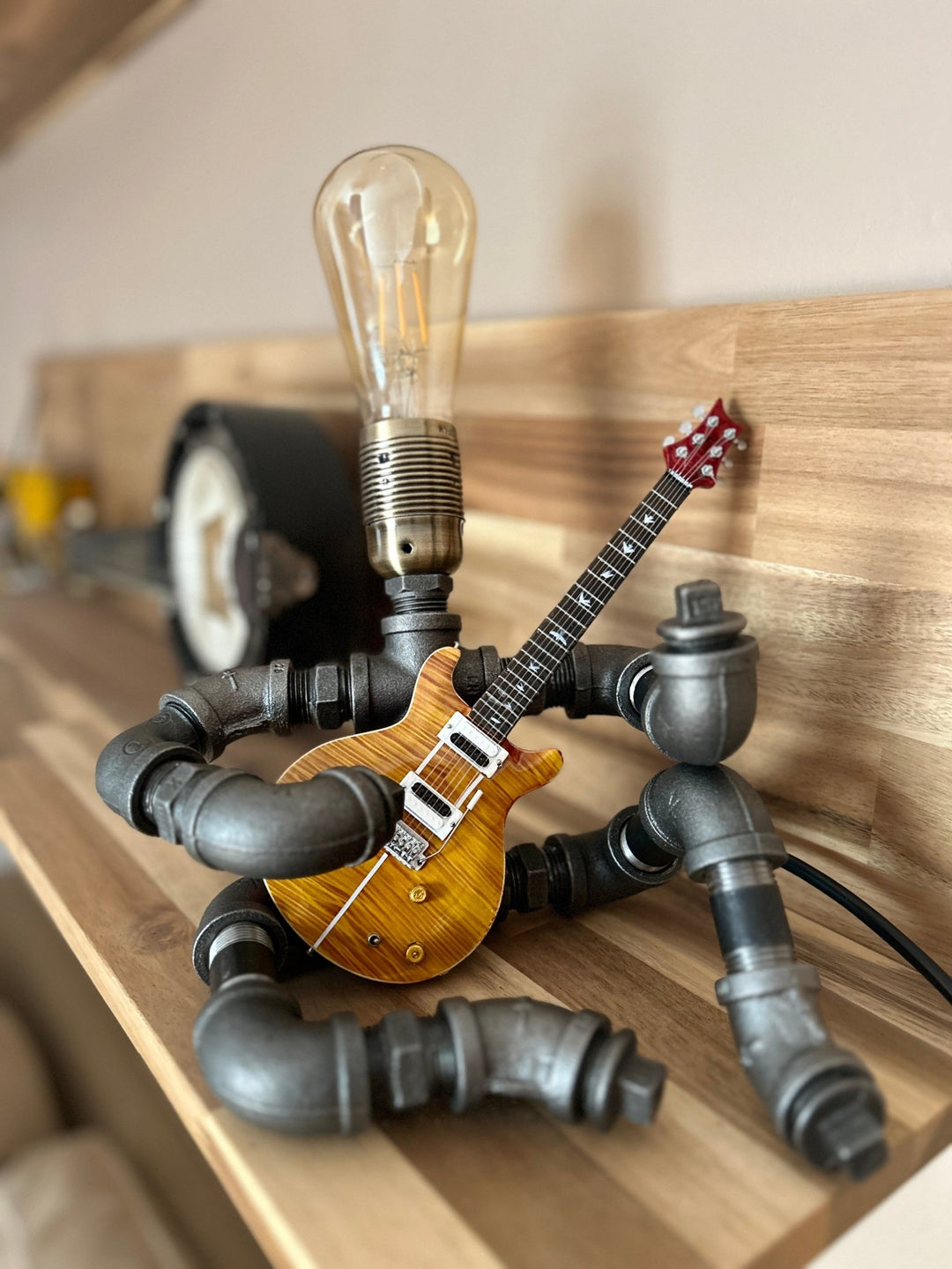 Pipework Guitar lamp holding a Santana inspired miniature guitar seated on a wooden shelf