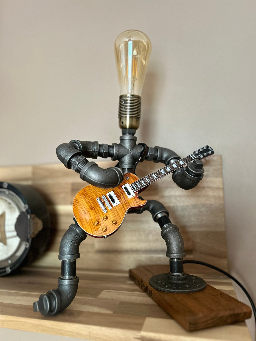 Guitar-shaped lamp made of pipes with a lit bulb on a wooden surface
