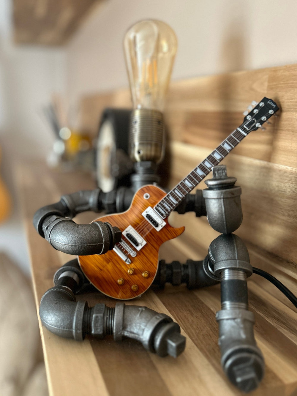 Pipework Guitar Lamp holding a Slash replica miniature guitar on wood background