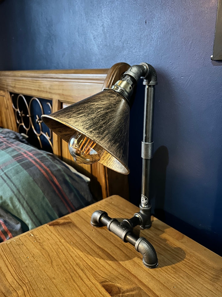 Industrial-style pipework bedside table lamp with a copper coloured shade on a bedside table