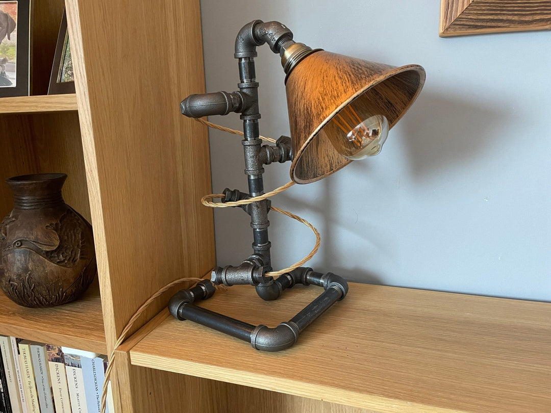 Pipework Lamp with braided gold cord spiralling around the lamp with copper coloured shade on a wooden shelf